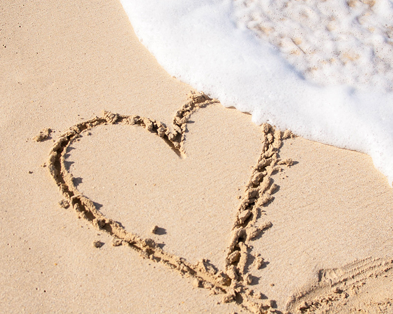 heart written in the sand by the ocean