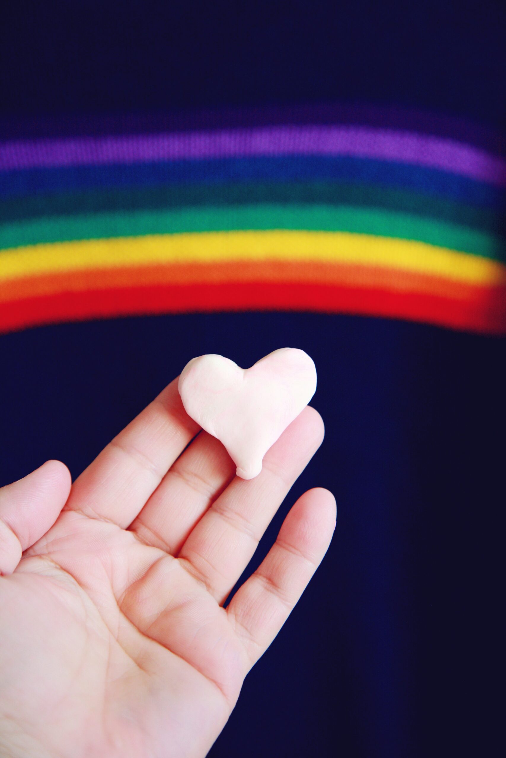 hand holding a small heart with rainbow in background