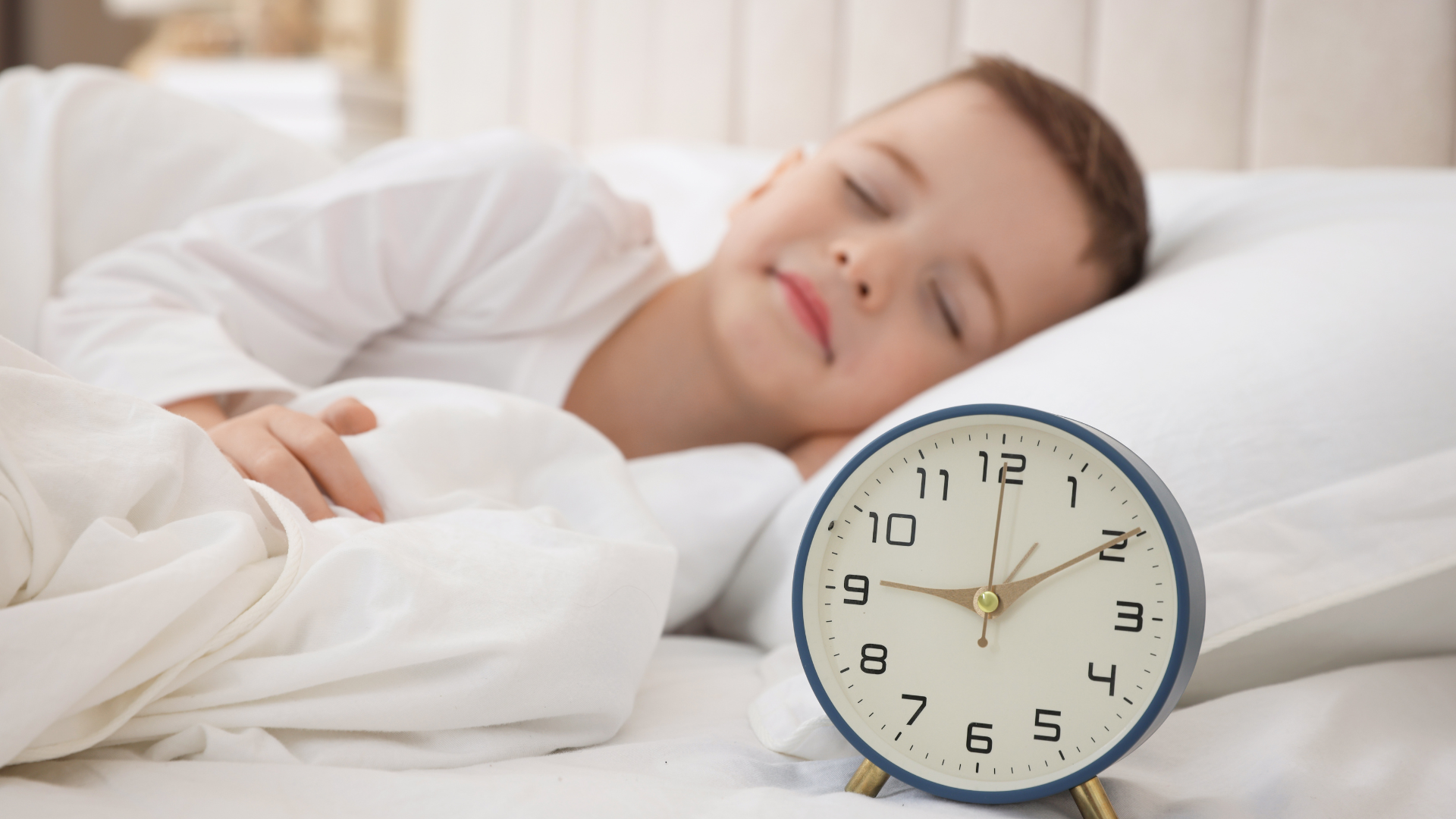 time change tips for kids boy sleeping in bed with alarm clock on bedside table