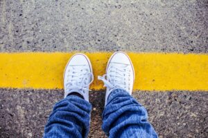person wearing converse shoes standing on yellow road line symbolizing setting healthy boundaries and protecting personal space
