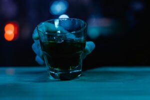 Hand holding a glass of alcohol in a dimly lit setting representing alcohol use, coping, and mental health awareness in Wisconsin