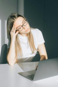 stressed young adult woman sitting at computer rubbing her face feeling overwhelmed and burned out