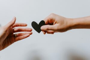 Two hands exchanging a black paper heart, symbolizing emotional support, connection, and compassionate mental health care during Mental Health Awareness Month in Madison WI.