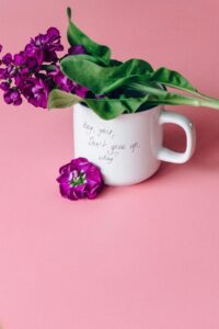 White mug with handwritten encouragement surrounded by purple flowers against a pink background, symbolizing hope, compassion, and emotional support during Mental Health Awareness Month in Madison WI.