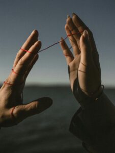 Two hands connected by red string, symbolizing family relationships, intergenerational connections, and patterns explored through genograms in trauma-informed therapy.