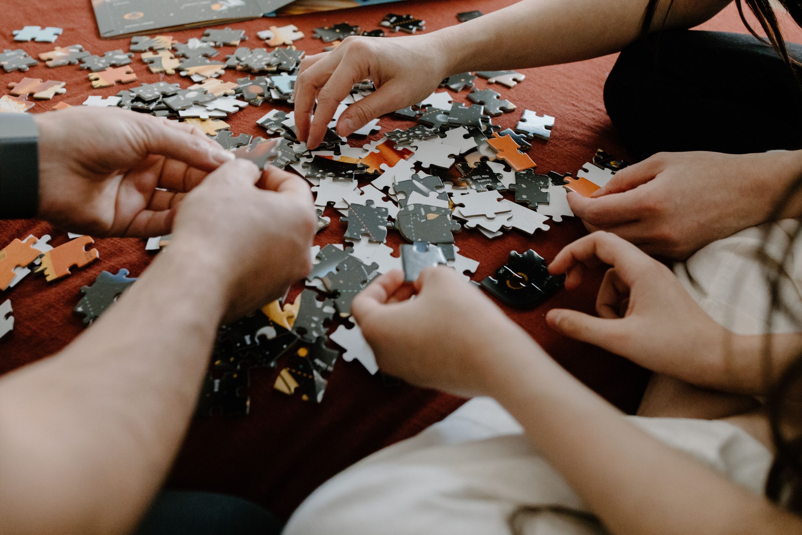 Parents and children reaching into a pile of puzzle pieces, symbolizing connection and collaboration in family therapy with Marriage and Family Therapists Madison WI.