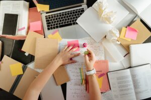 A woman working at her computer with a planner, calendar, or sticky notes nearby. This captures the constant tracking of appointments, schedules, and responsibilities described in the example of the invisible load that impacts women's mental health.