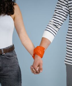 Couple holding hands with orange material wrapped around their wrists, symbolizing relationship control and trauma-informed therapy in Madison.